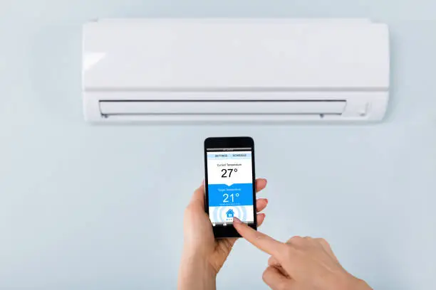 Close-up Of Person Hand Setting Temperature Of Air Conditioner Using Mobilephone At Home