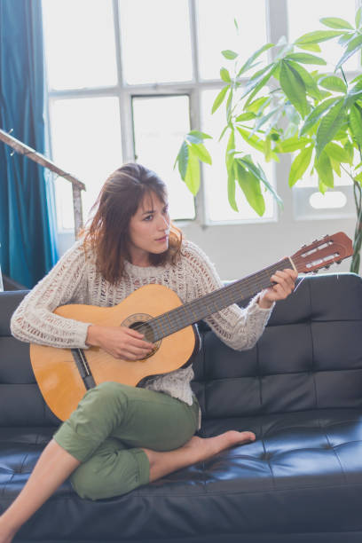 istock Beautiful young woman sitting on sofa playing guitar 854398466