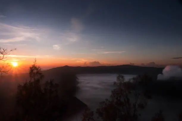 Mist hovering towards the active volcano Bromo in the morning during orange sunrise, at the Tengger Semeru National Park in East Java, Indonesia.