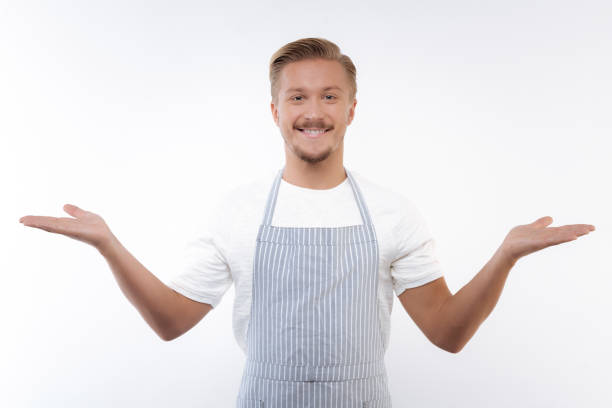 istock Cheerful man in apron spreading hands in welcoming gesture 854409722