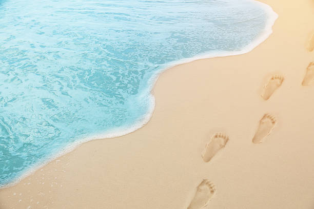 close up photography - Tropical Blue sea water coming on the white beach sand with footprint stock photo