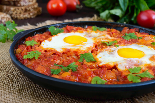 Shakshuka - a dish of eggs fried in a sauce of tomatoes, hot pepper, onions and seasonings. Israeli cuisine. Served for breakfast with rye bread.