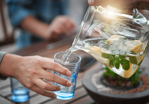 Shot of a unrecognizable person pouring water into a glass outside around a table