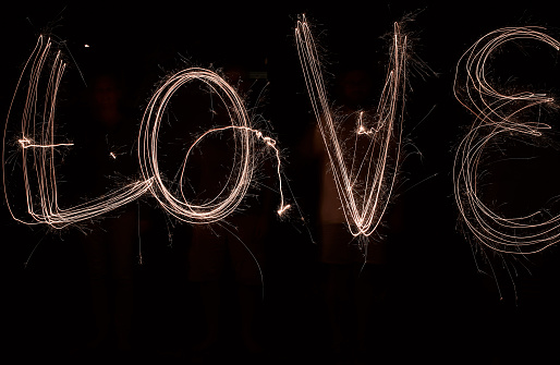 Shot of the word love being drawn with a sparkler through use of light painting outside at night