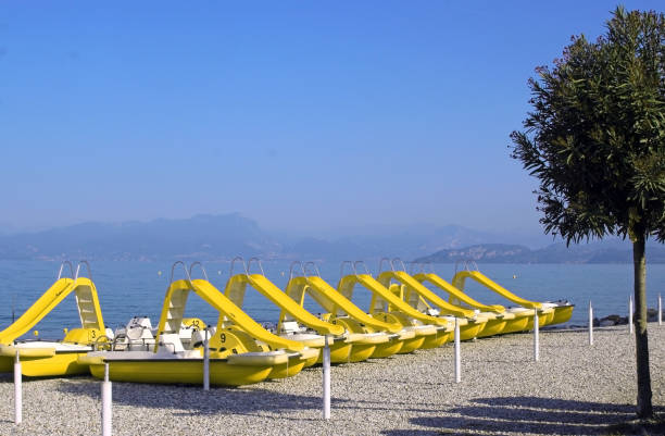 row of yellow pedal boats with slide at the beach of Peschiera, Lake Garda, Italy