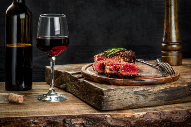 grilled ribeye beef steak with red wine, herbs and spices on wooden table - food and drink steak meat food imagens e fotografias de stock