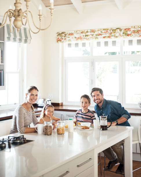 Breakfast - a time to nourish family bonds Portrait of a happy family of four having breakfast together in the kitchen at home nourish stock pictures, royalty-free photos & images