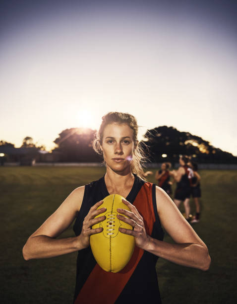 What? You were expecting a cheerleader? Portrait of a young woman holding a football on a field with her team in the background rugby players stock pictures, royalty-free photos & images