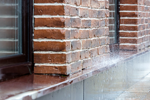 heavy rain pouring on pavement on red brick wall background