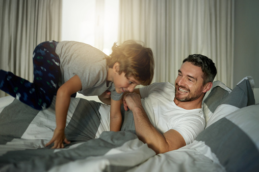Shot of a cute little boy jumping on his father’s bed in the morning