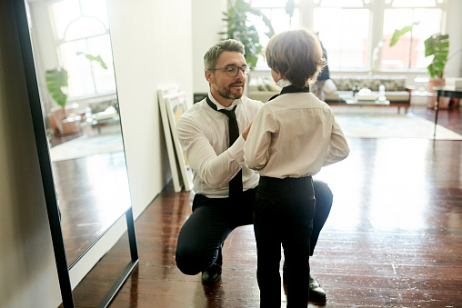 Shot of an adorable little boy and his father getting dressed in matching suits