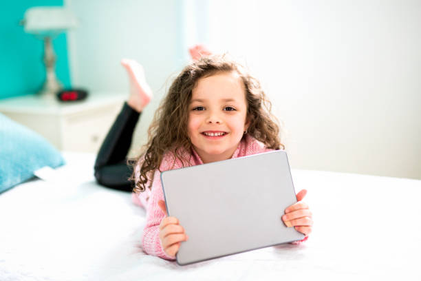 istock Technologies become easier. Cute little girl holding digital tablet and smiling while lying in bed 854468648