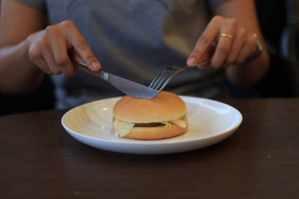 istock Woman prepare cutting burger in two halfs select focus, Holding cutting burger, Cutting burger in two halfs on table low light 854472942