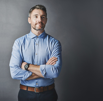 Studio shot of a handsome mature businessman looking contemplative while standing with his arms folded against a grey background