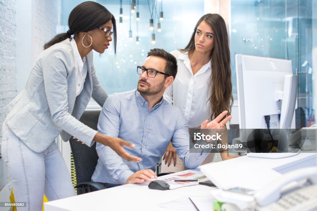 Group of three business people discussing some document on desktop computer in modern office. Emotional Stress Stock Photo