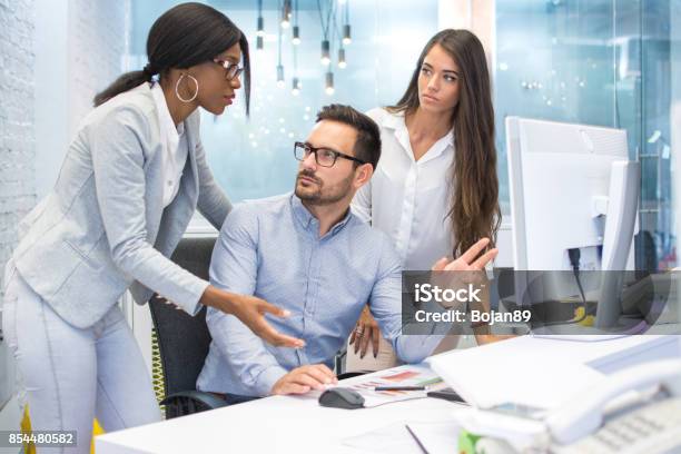 Group Of Three Business People Discussing Some Document On Desktop Computer In Modern Office Stock Photo - Download Image Now