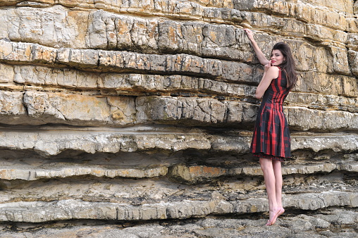 Young Brasil Women Portrait Outside on Rocks with red dress and without shoes.