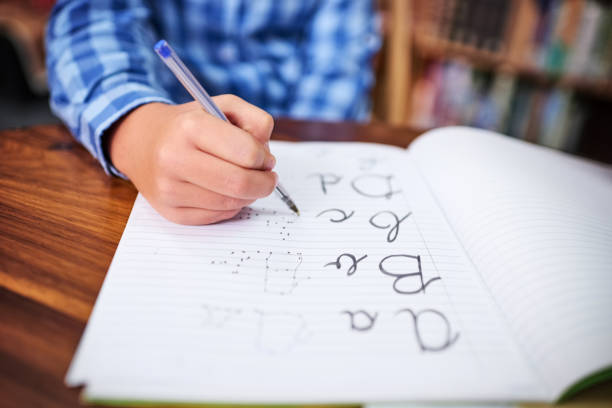 Practising his handwriting Shot of an unrecognisable young boy writing in a book at school spelling education photos stock pictures, royalty-free photos & images