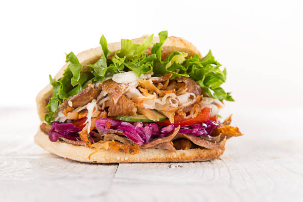 The image shows a Turkish-style meat sandwich prepared with sliced beef, tomatoes, onions and fresh herbs, all placed inside a soft flatbread. Served on a plate against a minimalist background, the dish reflects the traditional street food culture widely found in Turkish restaurants. The contrasting black and white setting helps highlight the colors and textures of the ingredients, making this composition ideal for menu layouts, branding visuals and promotional materials focused on authentic and flavorful cuisine.