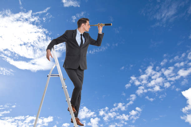 istock Businessman looking through spyglass from ladder 854593642