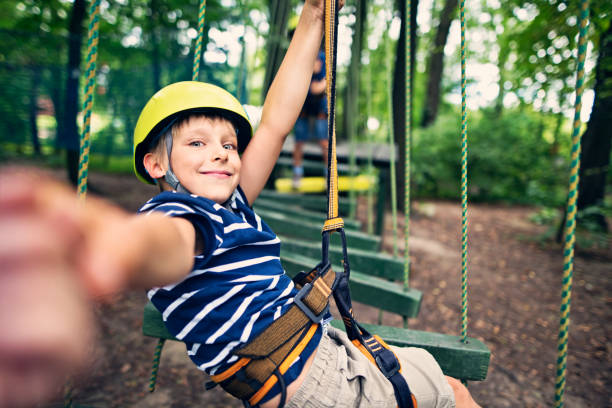 Little boys wearing helmets having fun during ropes course in adventure park. One of the boys is reaching for the helping hand.