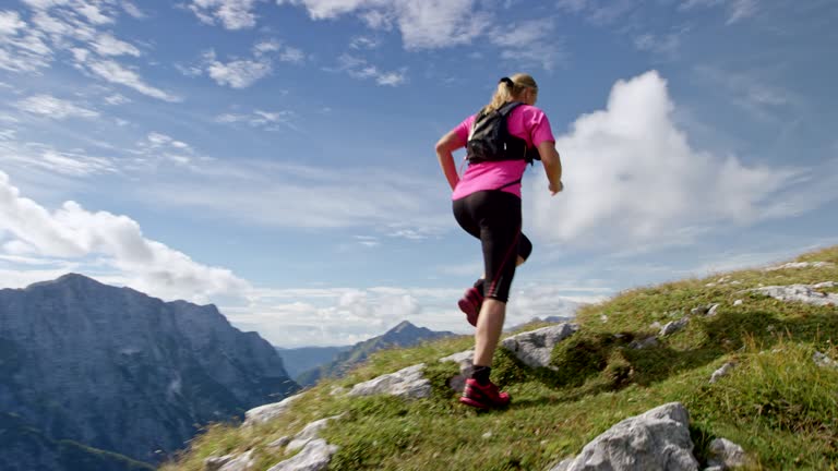 SLO MO Following a female runner running up a high mountain ridge in sunshine