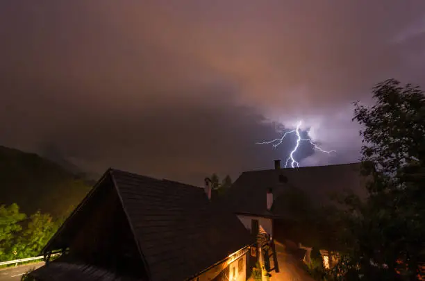 Lightning during a thunderstorm at night behind a farming house in the Austrian alps