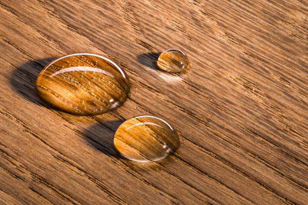 Three water beads on finished oak wood. Horizontal image.