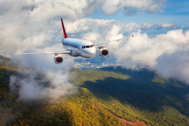 istock Airplane is flying in clouds over mountains with forest at sunset. Landscape with white passenger airplane, cloudy sky and green trees. Passenger aircraft is landing. Business travel. Commercial plane 854673970