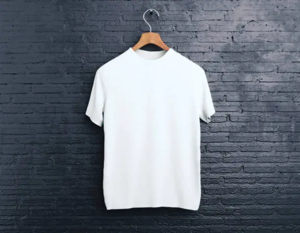 Wooden hanger with empty white t-shirt hanging on dark brick background. Shopping concept. Mock up. 3D Rendering