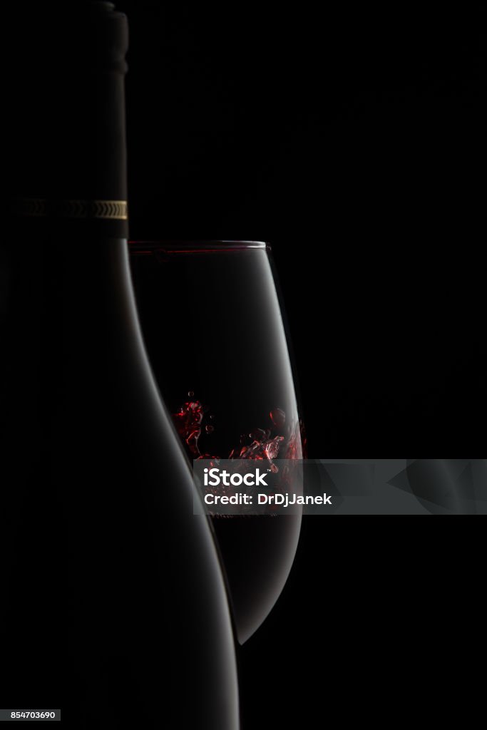 A bottle and glass of elegant red wine with splash. The silhouette of an unlabeled bottle and glass of elegant red wine with splash on the goblet, expressing luxury and stile, isolated on black. Wine Stock Photo