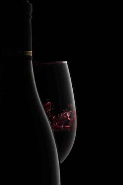 A bottle and glass of elegant red wine with splash. The silhouette of an unlabeled bottle and glass of elegant red wine with splash on the goblet, expressing luxury and stile, isolated on black. swirly vines stock pictures, royalty-free photos & images