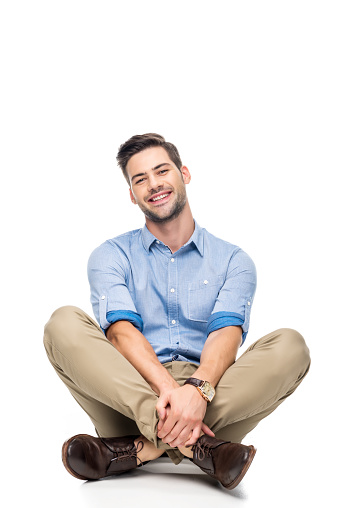 happy young man sitting on floor with crossed legs isolated on white