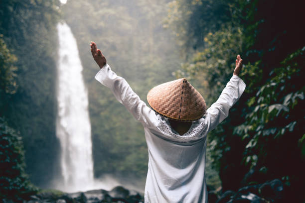 istock Asian Female with Raised Hands Praying by the Waterfall 854729860