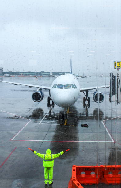 l'equipaggio di terra dirige un aereo in arrivo in posizione per incontrare un ponte a getto. - runway airport rain wet foto e immagini stock