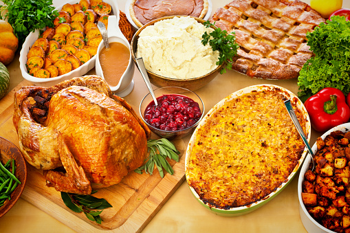 An overhead high angle photo of the Thanksgiving, Christmas dinner table with roast turkey with stuffings, mashed potatoes, green beans, corn gratin, baked sweet potatoes, gravy, cranberry sauce, pumpkin pie, and apple pie
