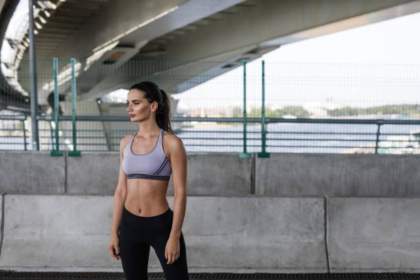 istock Young woman standing under a bridge, relaxing during workout 854741100