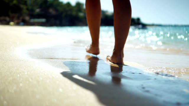 Close-up video of woman legs walking on the beach in shallow water.