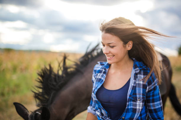 27 years old woman is walking with her horse. She loves to spend free time with him in the nature near the farm