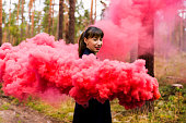 Young woman in forest having fun with red smoke grenade, bomb