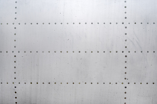 Aluminum surface of the aircraft fuselage. Smooth rows of rivets, there are scratches, dirt.