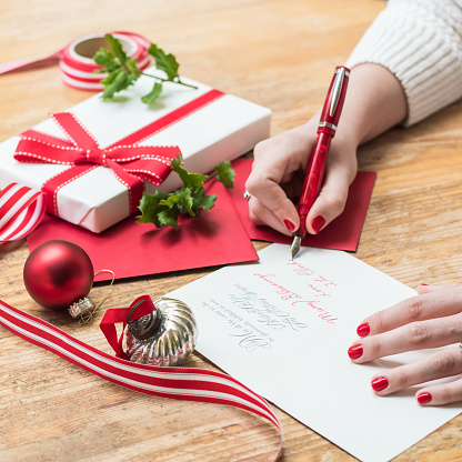 mujer joven escribiendo tarjetas de Navidad con uñas rojo, un bolígrafo rojo y decoraciones navideñas photo