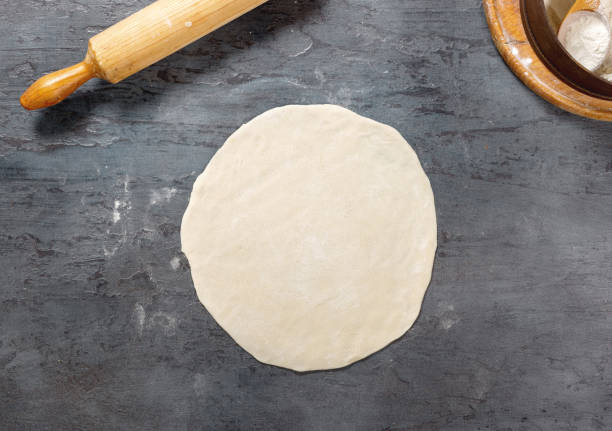 istock Raw pizza dough on a dark surface in a bakery close up 854894592