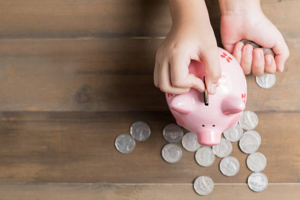 kid put coin to piggy bank on the vintage wood background kid put coin to piggy bank on the vintage wood background, a saving money for future education concept and copy space for input text. piggy bank finance currency savings stock pictures, royalty-free photos & images