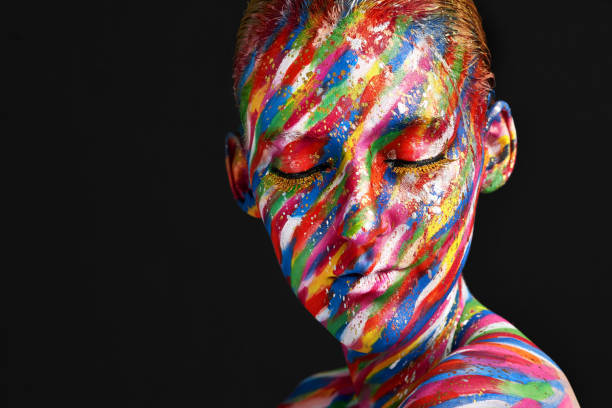 Studio shot of a young woman posing with brightly colored paint on her face against a black background