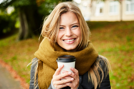 Smiling beauty with coffee in park, portrait
