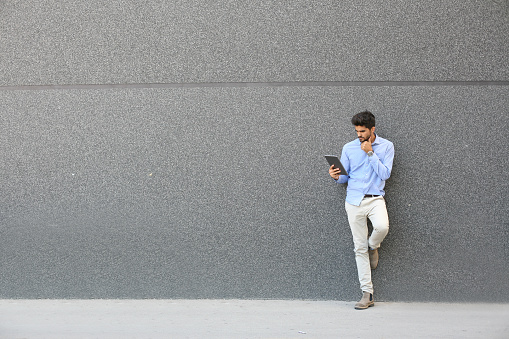 Joven empresario apoyado contra la pared con tableta digital.  Hombre de negocios utilizando el iPod en la calle. photo