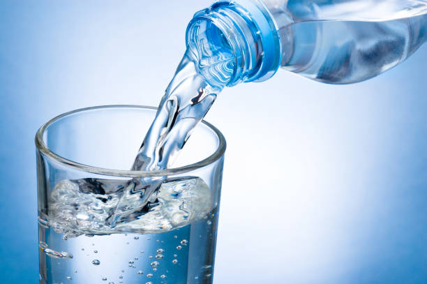 istock Pouring water from bottle into glass on blue background 854961654