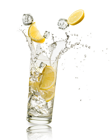 glass full of water with lemon slices and ice cubes falling and splashing water, on white background