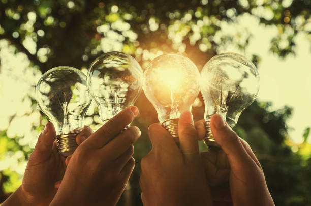 istock solar energy concept hand group holding light bulb in nature 854980942